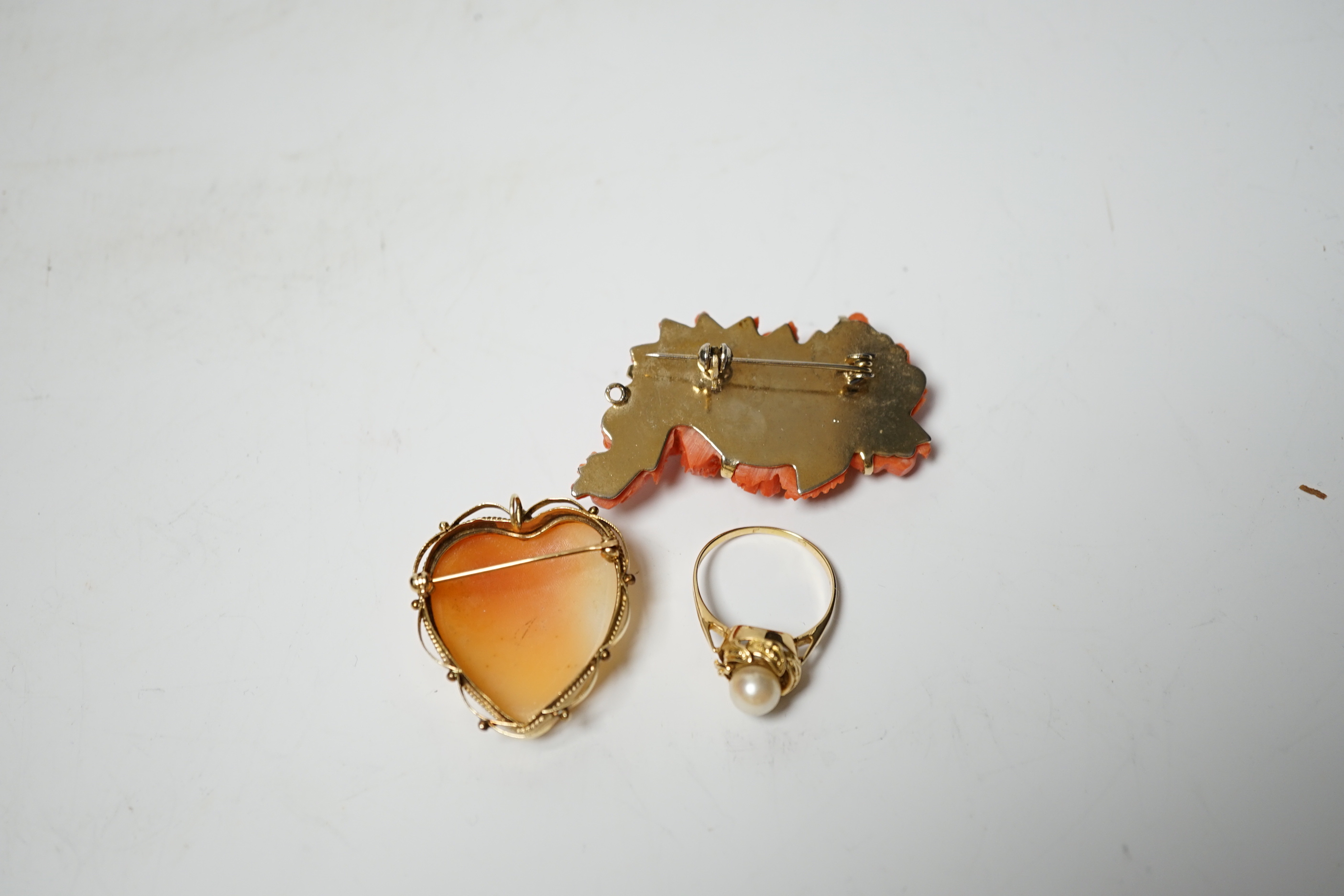 A 14k mounted heart shaped cameo shell pendant brooch, 33mm, a yellow metal and single stone cultured pearl set ring and a coral brooch.